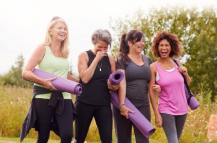 Four woman laughing and walking with their yoga mats